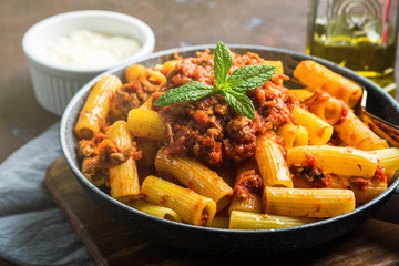Delicious rigatoni pasta with italian tomato meat ragu sauce served in a pan on dark brown background. Traditional pasta dish concept. Home made lunch - 337217247