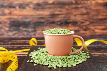 Cup with green coffee beans and measuring tape on table