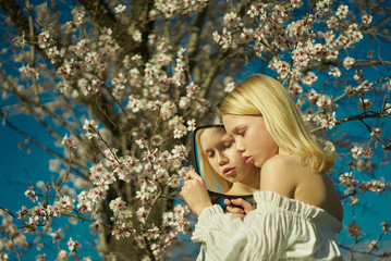 girl in a white dress see her reflection in the mirror on the background of a blossoming tree