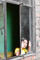 Serious little latin girl standing near window.
