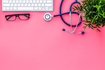 Stethoscope on doctor office desk. Pink background top view space for text