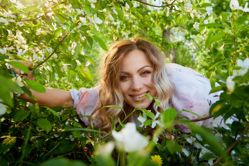 Portrait of a beautiful blonde girl with green eyes and blossoming apple tree with white flower in the park in a spring time