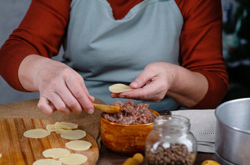Cook's hands sculpting dumplings from rolled dough discs and pieces of minced meat
