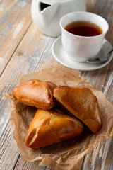 Traditional russian stuffed pierogi bake with golden crust, served on wooden table with a cup of tea