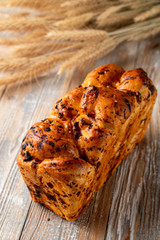 Rich bread with dried fruit and grated chocolate on top, served on wooden table with wheat spikes