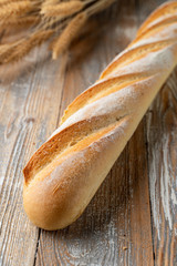 Sourdough french baguette, baked with golden crispy crust crust, white bread loaf on wooden background with wheat spikles around close up