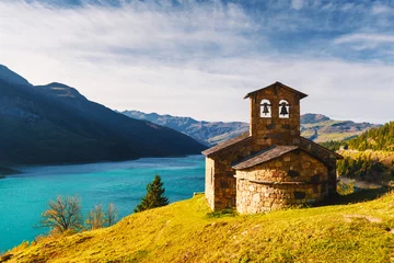 Gordijnen Sunny picturesque view of stone chapel on Roselend lake (Lac de Roselend) in France Alps (Auvergne-Rhone-Alpes). Landscape photography © Ivan Kmit