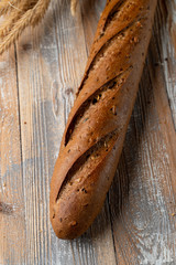 Whole grain rye baguette with seeds and sesame on wooden background with spikes around