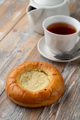 Brioche with sweet cottage cheese on wooden table with a cup of black tea