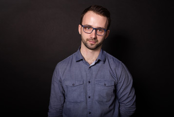Attractive brunette man in glasses confidently looks at camera. Black backgroung