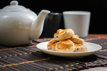 Cashew nut and black seasame cookies on white dish and wooden table with blurry pot of tea on black background. Afternoon tea concept.
