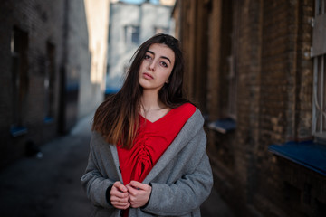 Girl in a red blouse and a gray cardigan on the background of the old brick wall