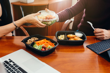 Male and female colleagues eat during a break at work. Share food in a container with each other.