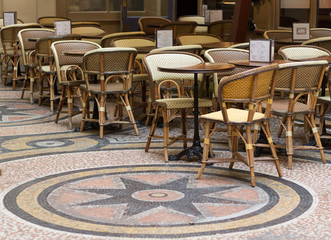 Outdoor seats and tables at a French Cafe in the center of Paris.  Tables and chairs with a beautiful mosaic floor. 