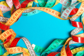 Top view of frame made of heap of colorful measure tapes on turquoise background. Keeping fit...