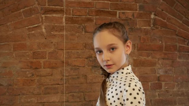 Beautiful girl teenager with braid posing front camera on brick wall background. Model girl teenager looking to camera and turning for shooting in brick studio