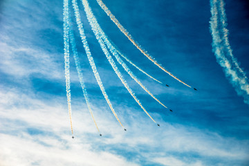 Group of seven small planes swirling down the blue sky and leaving the coloured smoked mark behind...
