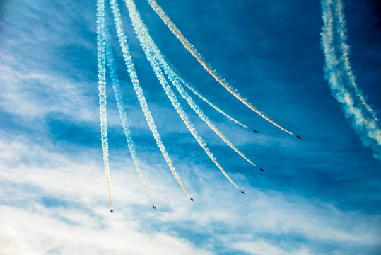 Group of seven small planes swirling down the blue sky and leaving the coloured smoked mark behind them. Airshow of small aircrafts making maneuvers in the sky