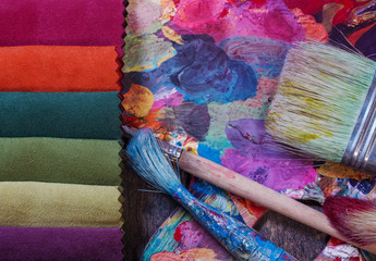 Colorfull textile lies on a colorfull palette of the artist. Colored brushes and fabrics.