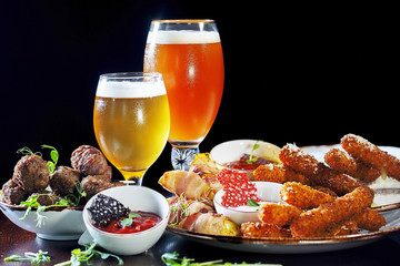 Beer set with lite and dark beer, sausages, red sauce, meat, lard, cheese sticks and snacks.  All products are on the table, on a black background.