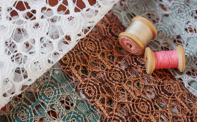 Wooden reels of pinl and white thread lie on brown, green and white lace. Beautiful textile.