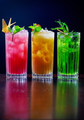  Lemonades with ice stand on a table on a black background and decorated with mint, lemon and limes.
