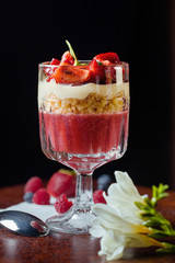 Delicios desert with strawberry and vanilla cream.Fresh berry with crushed nuts in glass cup.Professional and healthy food. Dessert stay close-up on a black background