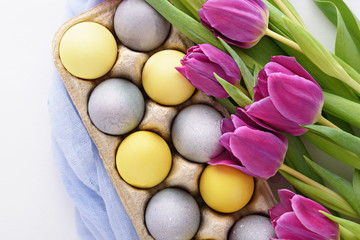 purple tulips and pastel yellow and blue Easter eggs on white background