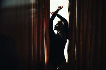 Silhouette of beautiful woman with arms raised up on light window background. Lifestyle, copyspace