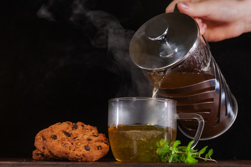 Hot green tea with mint is poured into a glass transparent Cup. There are cookies on the table
