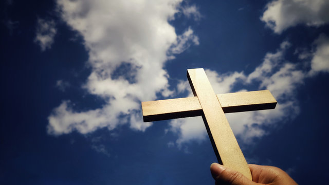 Lent Season,Holy Week and Good Friday concepts - image of wooden cross raise to the sky with hand holding it background
