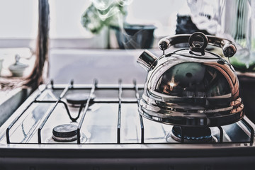 A metal silver teapot on a gas stove in front of the window. Boil water for tea