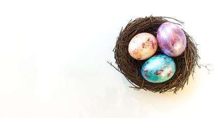 Obraz premium Three painted muticoloured pearlescent easter eggs in a bird nest isolated on white