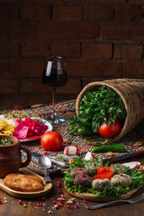 Traditional georgian meals, aubergine rolls, lobio boiled beans with spices, greens, tomato, cucumber and wine is served for lunch or dinner on wooden table.