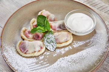 dumplings with berry filling, with sour cream laid out on plate decorated with mint leaves