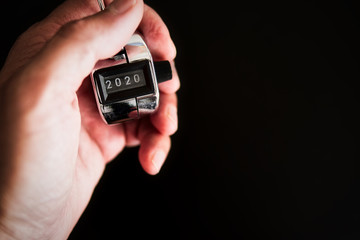 Close-up of a hand with a silver people counter standing in the year 2020 conceptually on a black background. Concept world recession by the coronavirus. Minimalist. Monochromatic. Complicated future