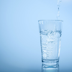 wasserstrahl beim eingießen in wasserglas vor abstraktem blauem hintergrund