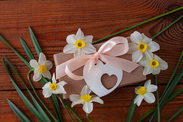 White daffodils and brown gift box, greeting card with pink ribbon on wooden background. Spring flowers around holidays present packaging. 8 March, Happy Birthday, Womens Mothers Valentines Day banner