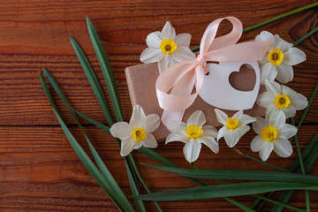 White daffodils and brown gift box, greeting card with pink ribbon on wooden background. Spring flowers around holidays present packaging. 8 March, Happy Birthday, Womens Mothers Valentines Day banner