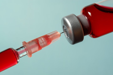 Syringe needle pierces the cap of medical vial with red liquid. Red liquid in syringe.