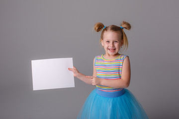 a little girl holding a sheet of white blank paper smiling on a white background