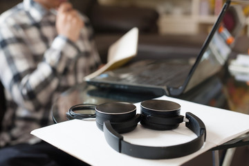 Headphone put on an empty book with a serious businessman on background metaphor working from home.