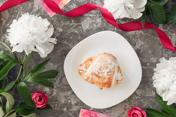 three white peonies with green stem and croissant on a gray stone background