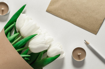 bouquet of tulips in craft paper, letter, pencil and candles on a white background