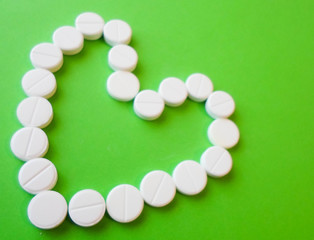 white pills on a green background in the shape of a heart. snow-white round antibiotics against viruses.
