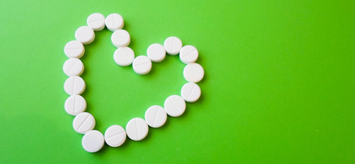 white pills on a green background in the shape of a heart. snow-white round antibiotics against viruses.