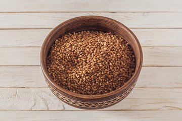 raw buckwheat in a brown clay plate on a white wooden boards