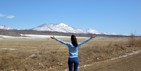 Slender brunette woman embracing  nature with open arms. The foot of the snowy mountains. concept of going out after quarantine. Russia, North Primorye.