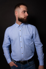 Caucasian man with beard looking to the side, hand in pocket. Black background
