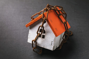 A toy house wrapped in a chain on a dark background. The concept of the arrest of property for tax...